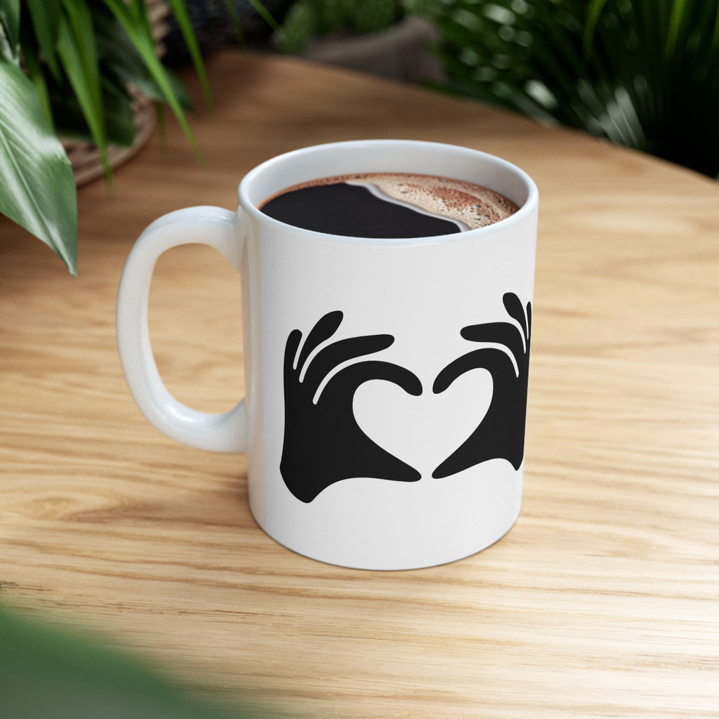 White mug with black hand and heart design on a wooden table