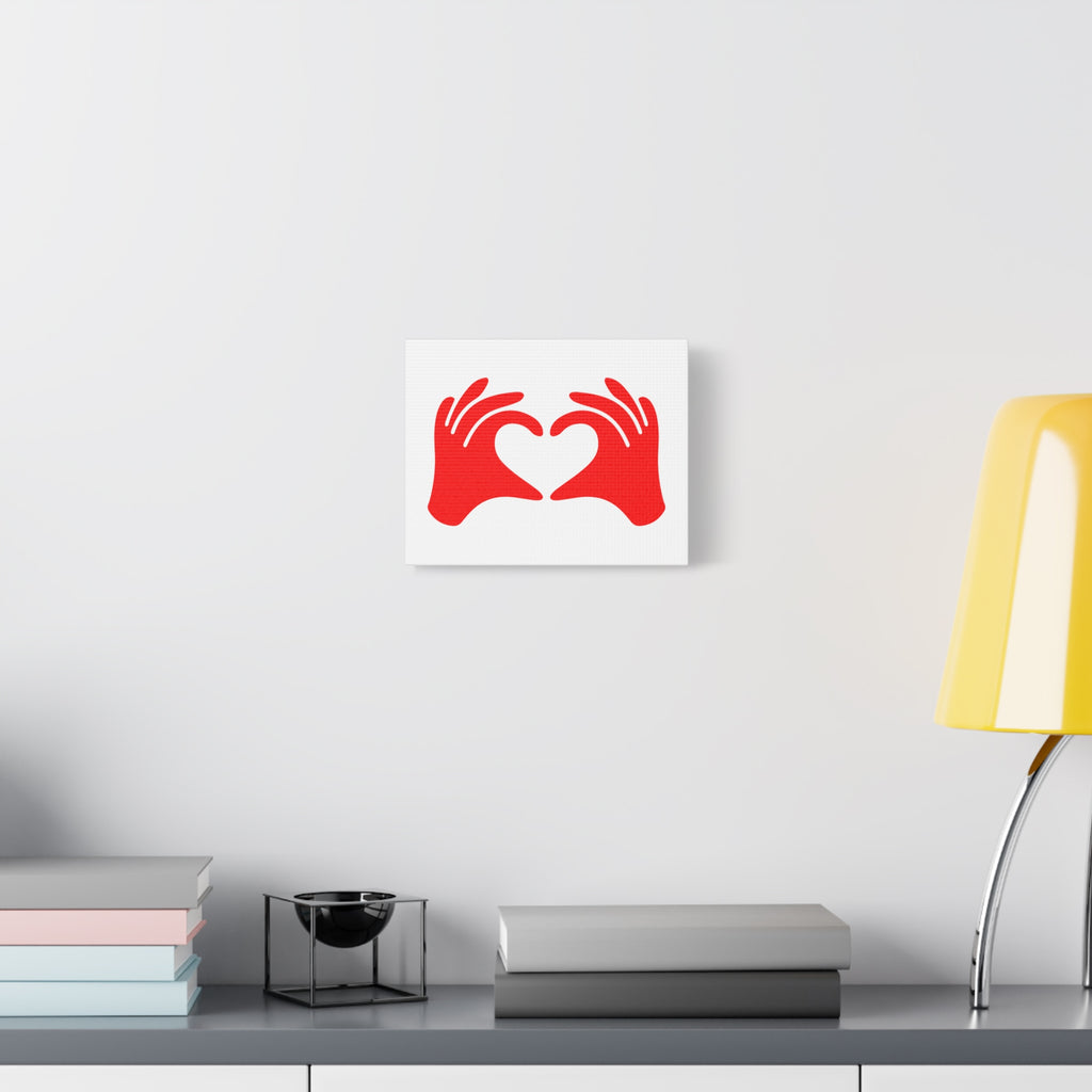 Decorative wall art with red hands holding a heart on a white background, displayed on a wall above a desk.