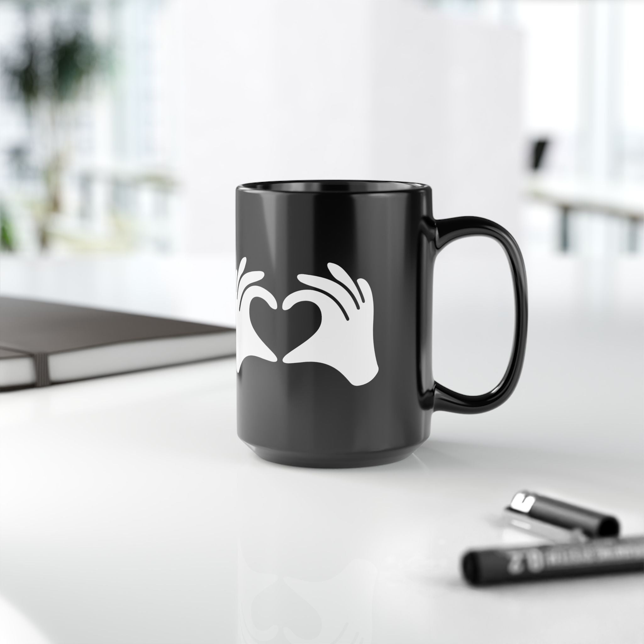 Black mug with a white heart and hand design on a blurred office background