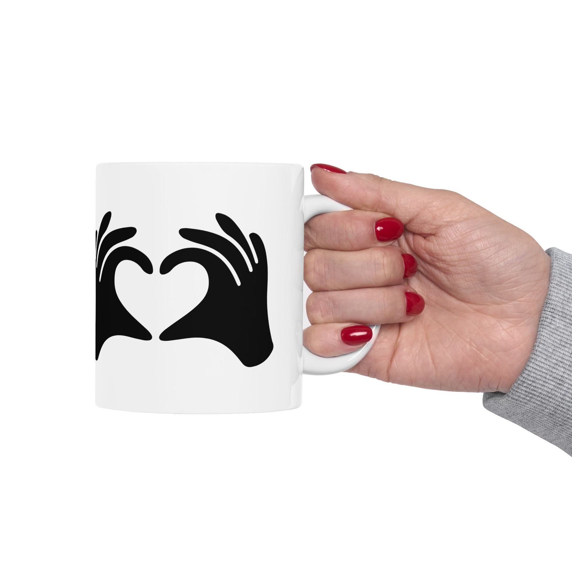 White mug with black heart design held by a hand with red nail polish on a white background
