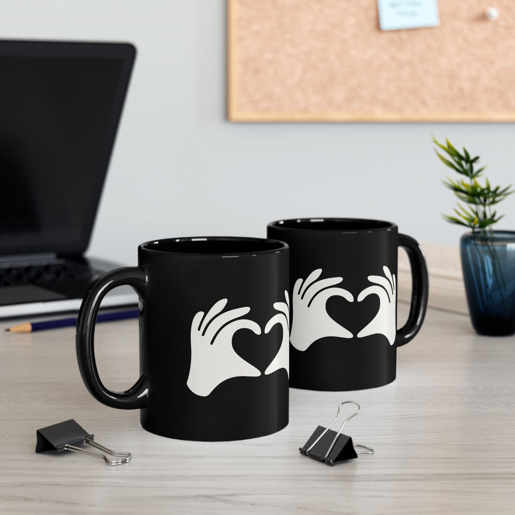 Two black mugs with heart designs on a desk with office items.