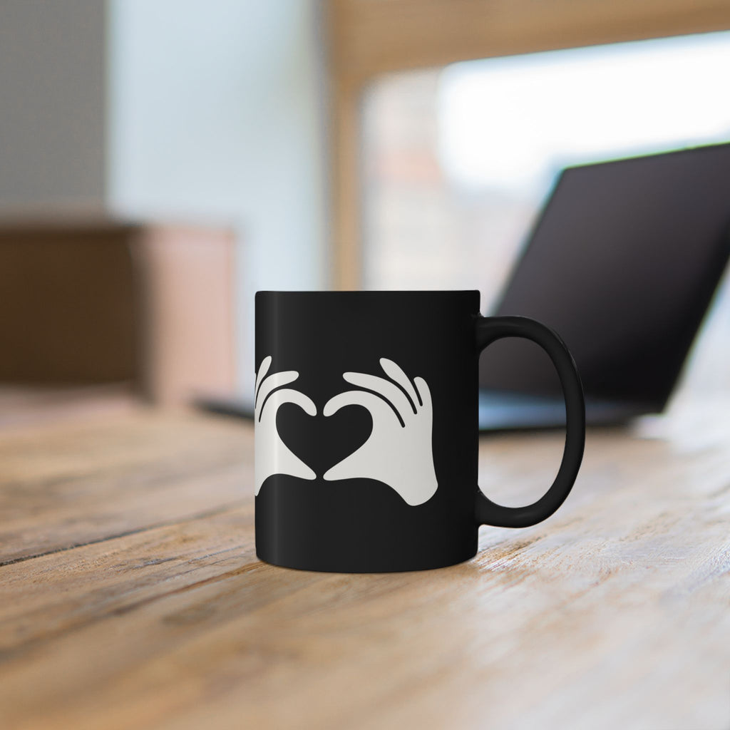 Black mug with white design of hands forming a heart on a wooden surface.